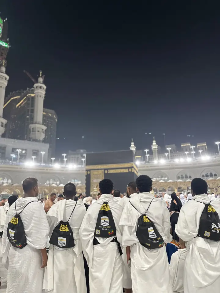 Pilgrims with Muhrim bags standing before the Kaaba at night