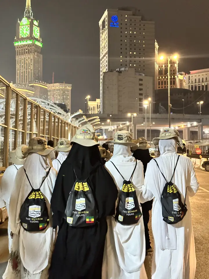 A Muhrim group walking in ihram towards the Makkah clock tower at night